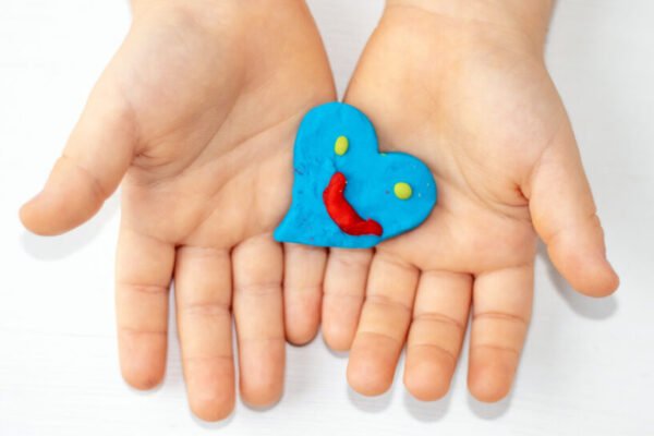 kid mother woman hands with red clay plasticine hearts shape in palm.many colored hearts on table blue yellow colour smiley face emoticon