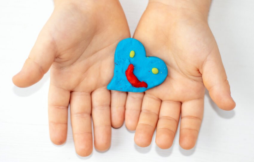 kid mother woman hands with red clay plasticine hearts shape in palm.many colored hearts on table blue yellow colour smiley face emoticon