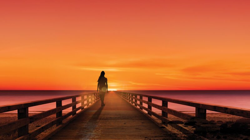 Silhouette of a woman on a jetty at sunset by the sea